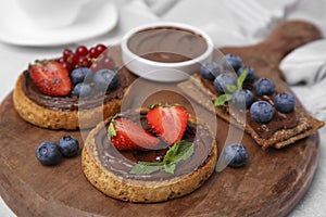 Tasty organic rusks and crispbreads with toppings on wooden board, closeup