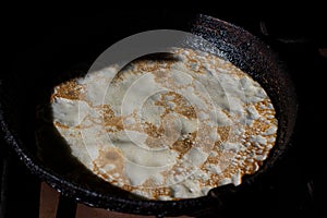 Tasty pancake in a cast-iron pan. Fry a delicious pancake in a rustic cast iron skillet. Traditional old Russian home