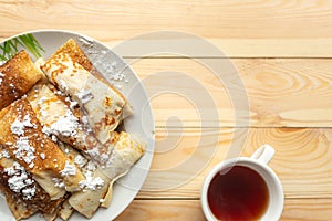 Tasty pancake rolls and tea cup on wooden table, top view