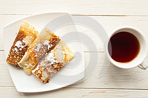 Tasty pancake rolls and tea cup on wooden table, top view