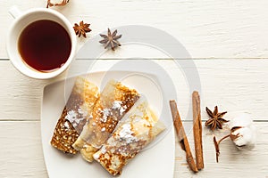 Tasty pancake rolls and tea cup on wooden table, top view