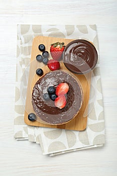 Tasty pancakes with chocolate paste and berries on white wooden table, top view