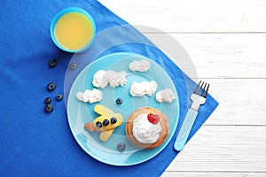 Tasty pancakes served with berries, whipped cream and juice on white wooden table. Creative idea for kids breakfast