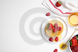 Tasty pancakes served with fresh berries and honey on white table, flat lay. Space for text
