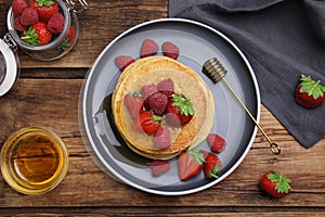 Tasty pancakes served with fresh berries and honey on wooden table, flat lay
