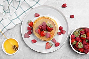 Tasty pancakes served with honey and berries on light grey table, flat lay