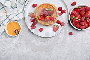 Tasty pancakes served with honey and berries on light grey table, flat lay. Space for text