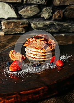 Tasty pancakes with strawberries, syrup, sugar and bacon on the top - darke background. Pancakes with fruits on dark wooden table