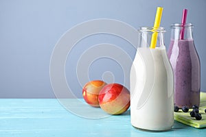 Tasty peach and blueberry milk shakes in bottles on light blue wooden table