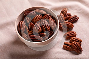 Tasty pecan nuts with bowl on beige cloth, closeup