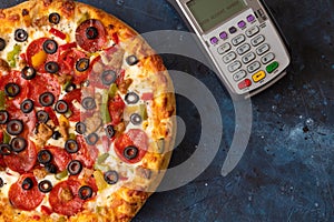 Tasty pepperoni pizza with terminal for payment, service on a blue concrete background. Top view of hot pepperoni pizza. Banner