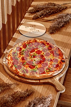 Tasty pepperoni pizza on a traditional wooden plate. Wooden background, top view