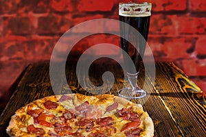 Tasty pepperoni pizza on wooden table near a glass of dark beer