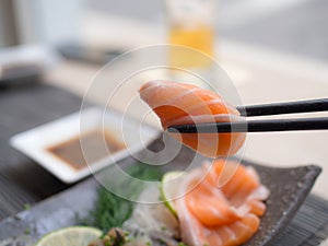 A tasty piece of salmon sashimi on chopsticks.