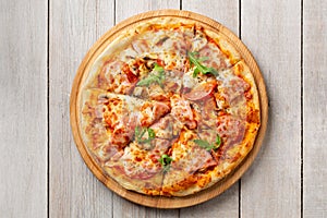 Tasty pizza with ham, mushrooms, tomatoes and arugula on wooden cutting board on white background.