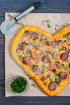 Tasty pizza in a heart shape with mushrooms, salami, pepperoni, olives, corn.