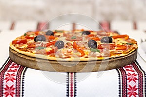 Tasty pizza with vegetables, basil, olives, tomatoes, green pepper on cutting board, table cloth traditional colorful