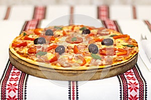 Tasty pizza with vegetables, basil, olives, tomatoes, green pepper on cutting board, table cloth traditional colorful