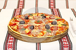 Tasty pizza with vegetables, basil, olives, tomatoes, green pepper on cutting board, table cloth traditional colorful