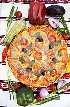 Tasty pizza with vegetables, basil, olives, tomatoes, green pepper on cutting board, table cloth traditional colorful