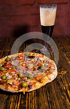 Tasty pizza on wooden table near a glass of dark beer