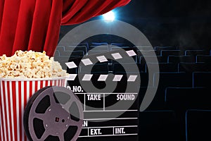 Tasty popcorn, film reel and clapperboard under red main curtain in cinema, space for text