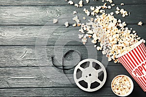 Tasty popcorn and film reel on wooden background, top view with space for text