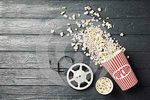 Tasty popcorn and film reel on wooden background, top view with space for text.