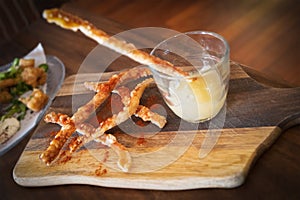 Tasty pork crackling strips and an apple sauce dip in a glass on a wooden board served as a snack or appetiser photo