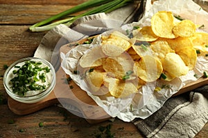 Tasty potato chips with sour cream and herbs on wooden background