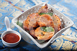 tasty potato fritters. aloo chops. aloor chops. potato cutlet.aloo tikki in a white plate with curry leaves and red chutni