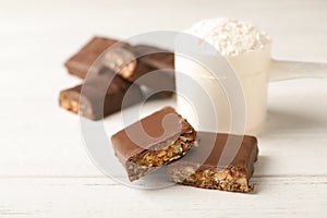 Tasty protein bars and scoop of powder on white table.