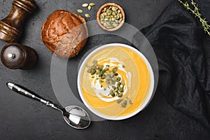 Tasty pumpkin cream soup in bowl over black background