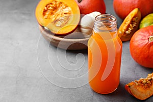 Tasty pumpkin juice in glass bottle and different pumpkins on light grey table. Space for text