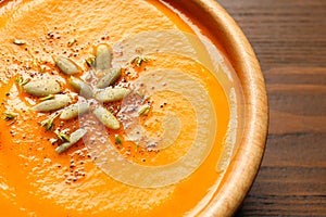 Tasty pumpkin soup with seeds in bowl on wooden table