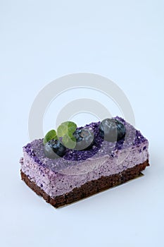Tasty purple blueberry mousse cake with blueberry and mint leaves on white background, vertical, side view, copy space