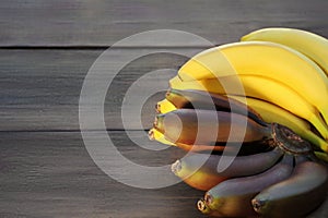 Tasty purple and yellow bananas on wooden table, space for text