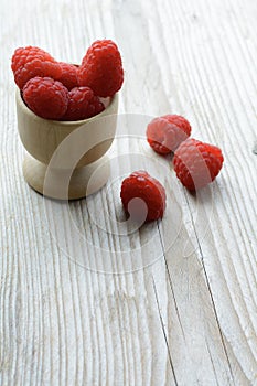 Tasty raw raspberries are in the wooden cup and on the wooden background. Healthy raspberries