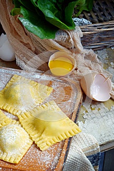 Tasty raw ravioli with ricotta and spinach, with flour and eggs on wooden background. Process of making italian ravioli.