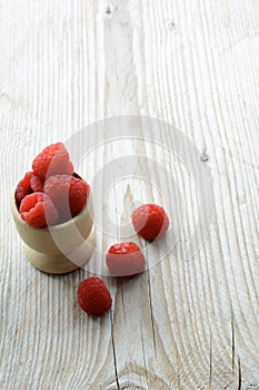 Tasty red fresh raspberries are in the wooden cup and on the wooden background. Healthy raspberries