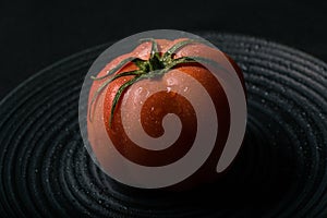 Tasty red tomato on a black plate.