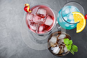 Tasty refreshing cocktails in glasses on grey stone table, flat lay.