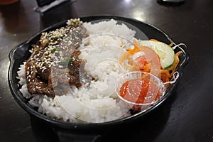 Tasty rice with beef teriyaki with chopped vegetables and chili sauce on a black plate