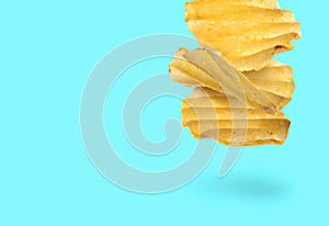Tasty ridged potato chips falling on cyan background, space for text