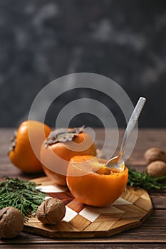 Tasty ripe persimmons with walnuts and cutting board on wooden table