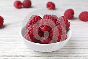 Tasty ripe raspberries in bowl on white wooden table, closeup