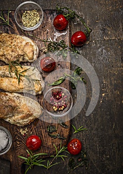 Tasty roasted chicken fillet with herbs,spices,seasoning and tomatoes on vintage gutting board over rustic wooden background, top