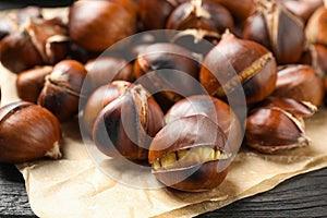 Tasty roasted edible chestnuts on black wooden table, closeup