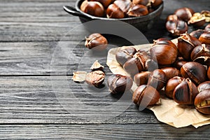 Tasty roasted edible chestnuts on black wooden table, closeup. Space for text