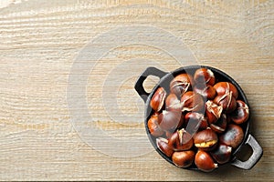 Tasty roasted edible chestnuts on wooden table, top view. Space for text